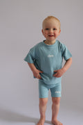Child wearing a light blue outfit with 'rivv' branding on a plain background