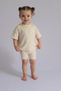 Child wearing a beige t-shirt and shorts set on a plain background