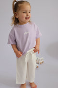 Child wearing a purple shirt and white pants on a plain background
