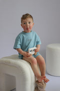 Child wearing a light blue shirt sitting on a white stool against a plain background